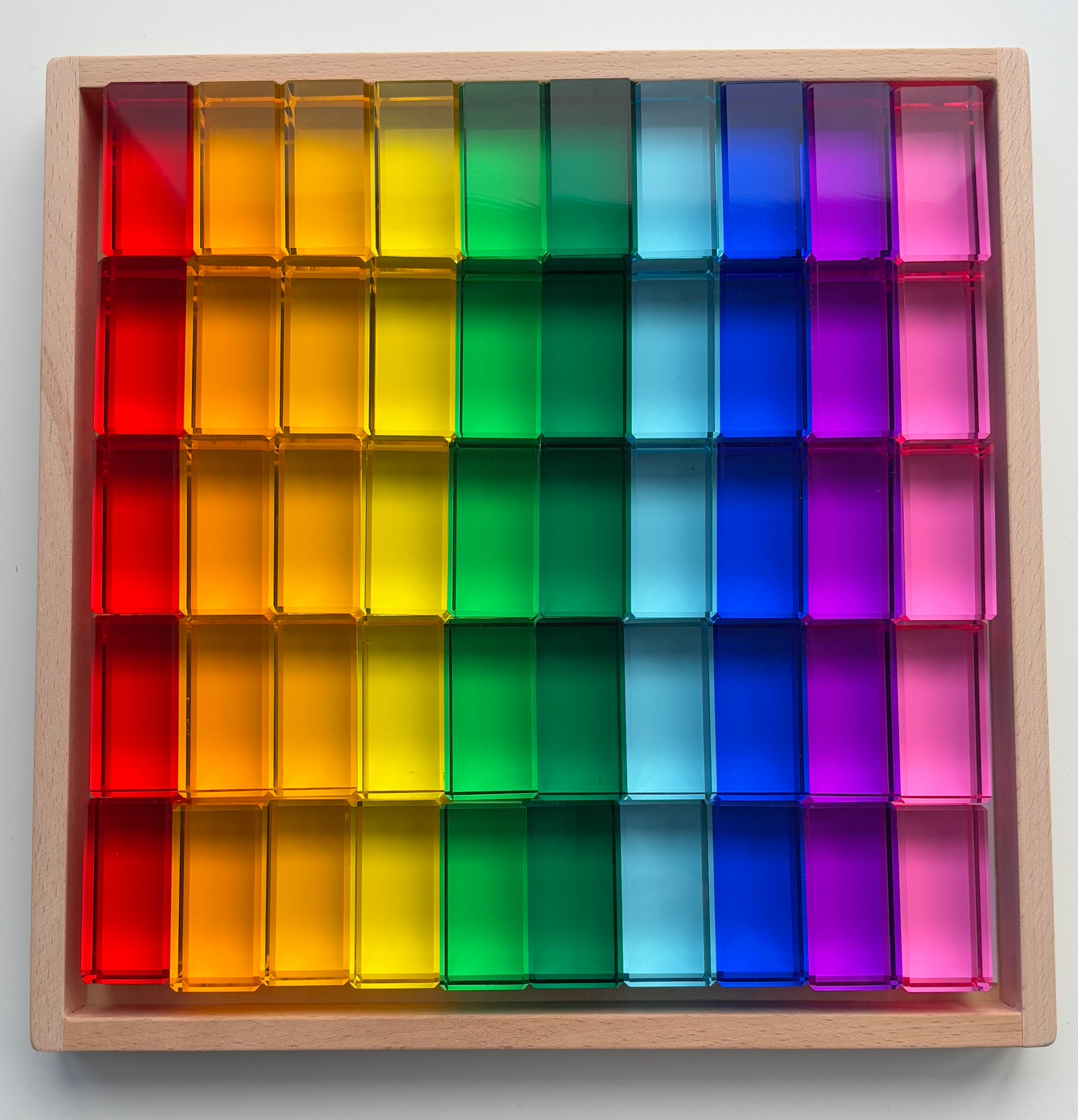 A set of transparent acrylic blocks in various colours of the rainbow, arranged in a rectangular frame. Infinite Wonder Acrylic Building Blocks - a great addition to any play space to build children's creativity and skill building.