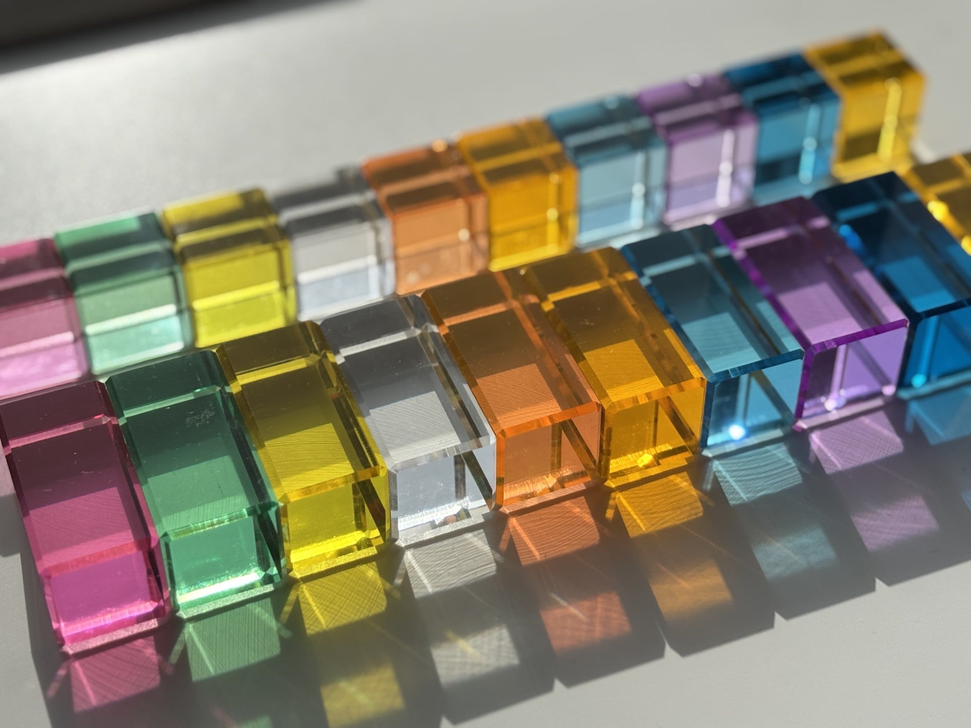 Pastel transparent acrylic blocks arranged in a pattern on a white surface, each colour reflects through the block on to the white surface.