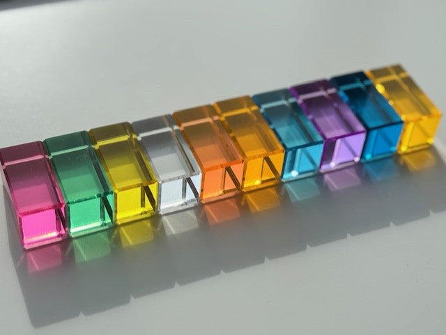 Pastel transparent acrylic blocks arranged in a pattern on a white surface, each colour reflects through the block on to the white surface.