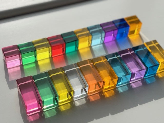 Pastel and rainbow transparent acrylic blocks arranged in a pattern on a white surface, each colour reflects through the block on to the white surface.