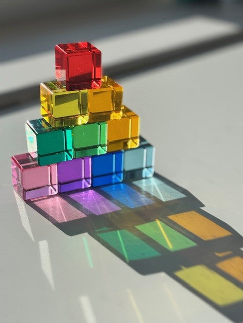 Stack of transparent coloured cubes casting a rainbow shadow on a reflective surface.